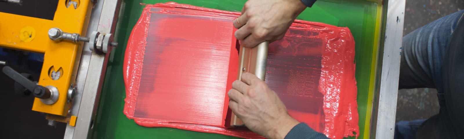 Hands pulling bright ink over a printing screen